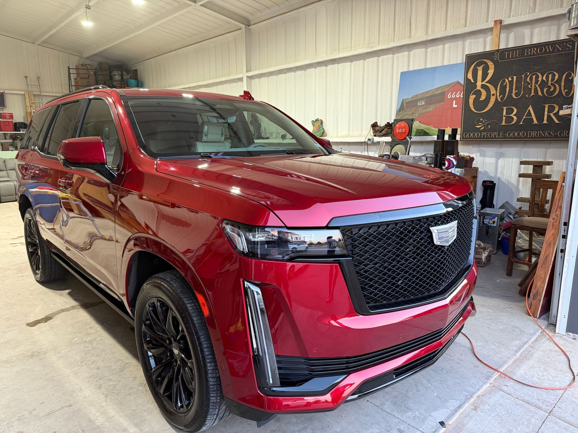 Red Cadillac Escalade SUV parked inside a well-lit garage. Black wheels and grill, with a 