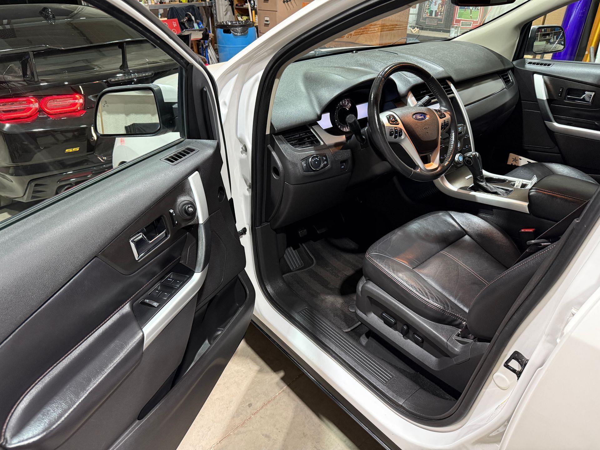 Interior of a white Ford Edge with the driver's side door open. Black leather seats and dashboard, showing steering wheel and center console.