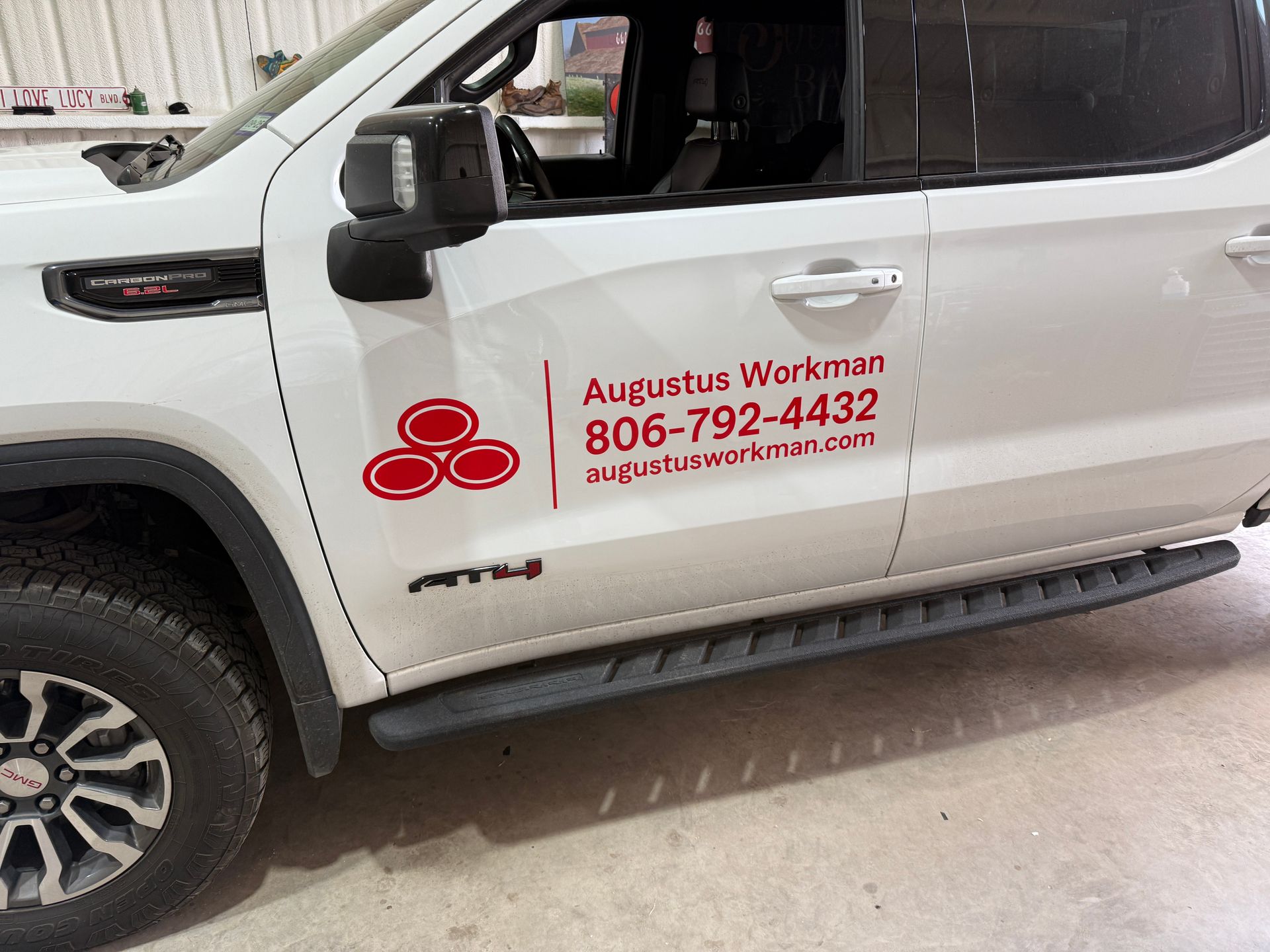 White GMC truck with red company logo and contact information on the side, parked indoors.