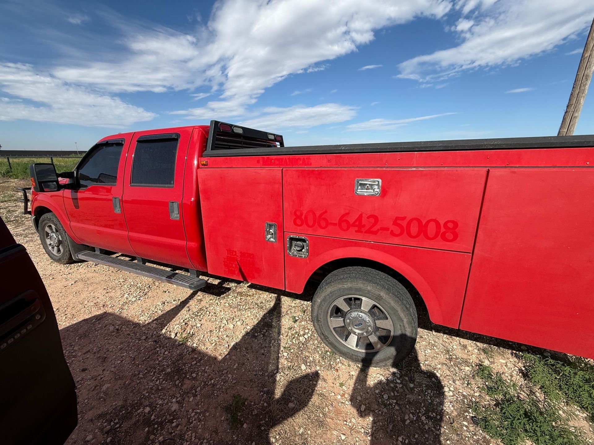 Red service truck parked on a dirt road with a phone number.