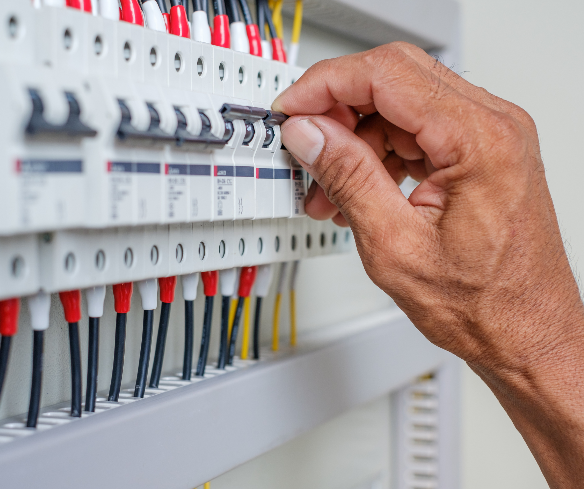 Hand flipping a circuit breaker switch in a gray electrical panel with red and white wires.
