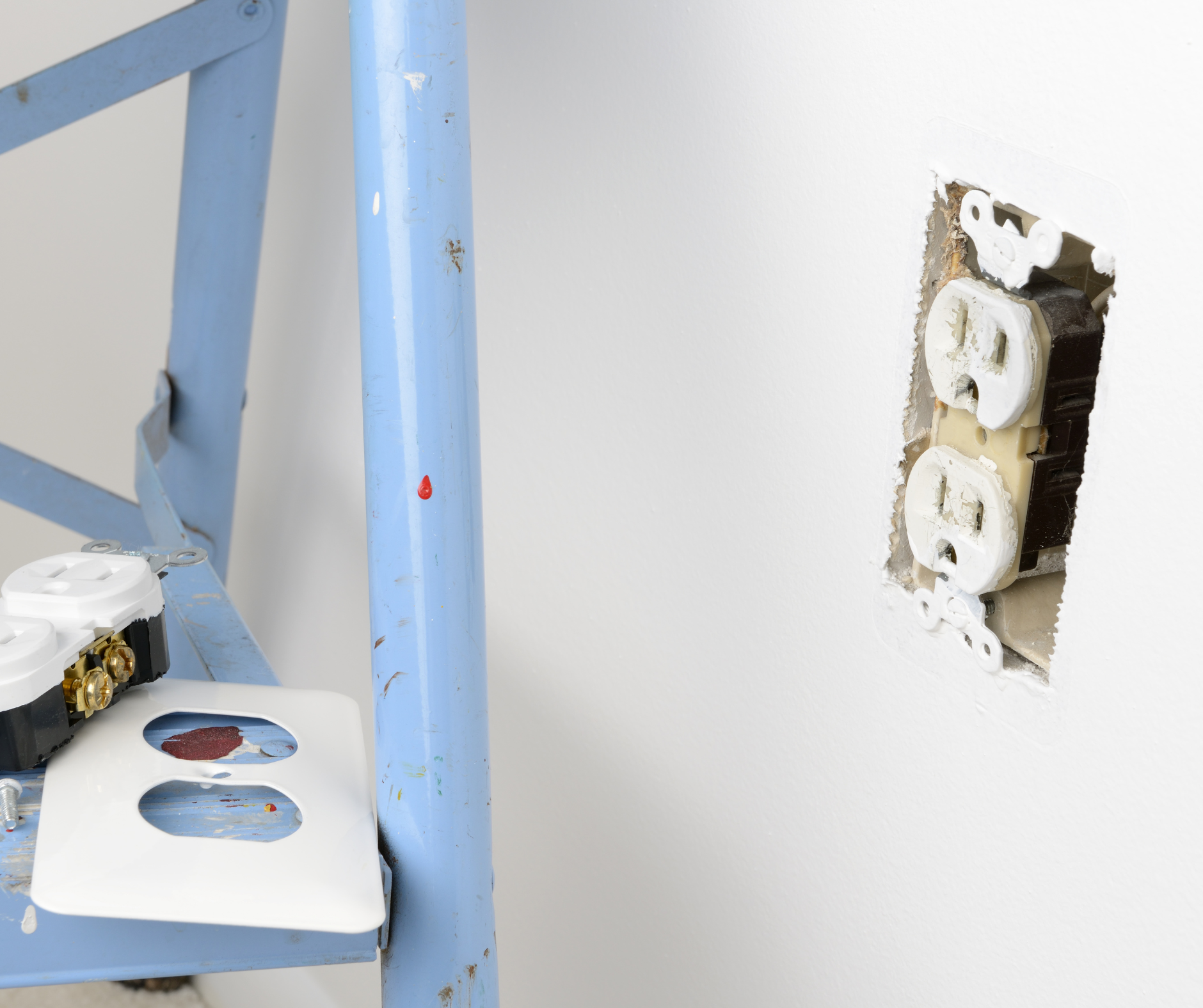 Blue ladder, exposed electrical outlet in wall, and replacement outlet components.