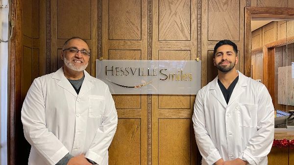 Two men in white coats are standing in front of a sign that says hessville smiles.