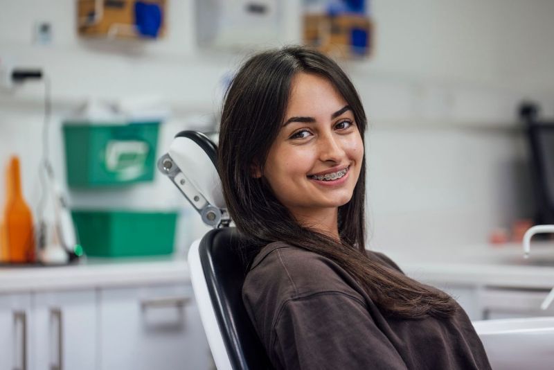 A woman with braces is sitting in a dental chair and smiling.