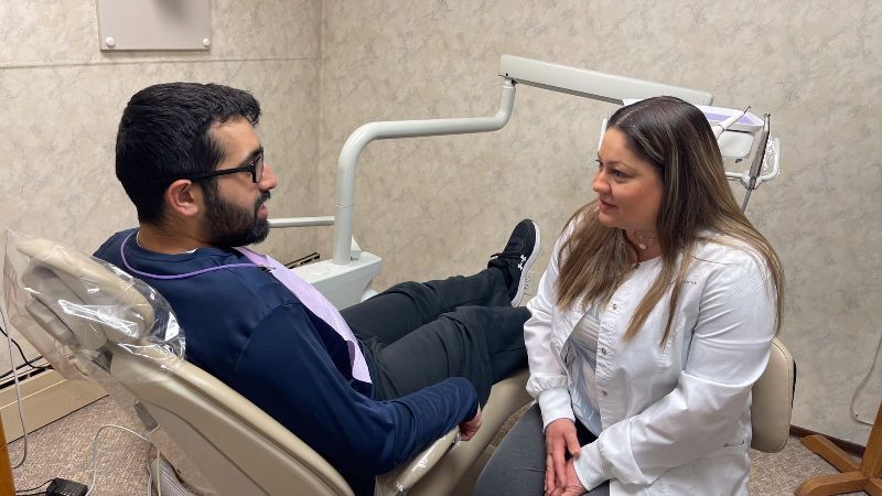 A man is sitting in a dental chair talking to a female dentist.