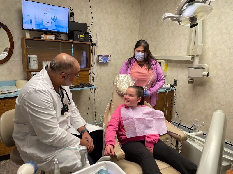 A girl is sitting in a dental chair while a dentist and a nurse look on.