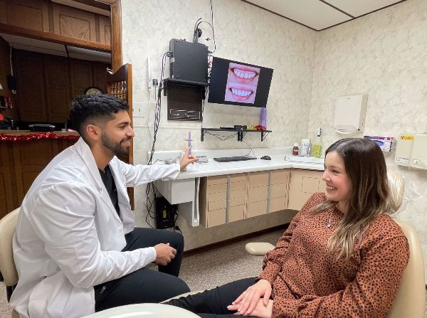 A dentist is talking to a woman in a dental chair.