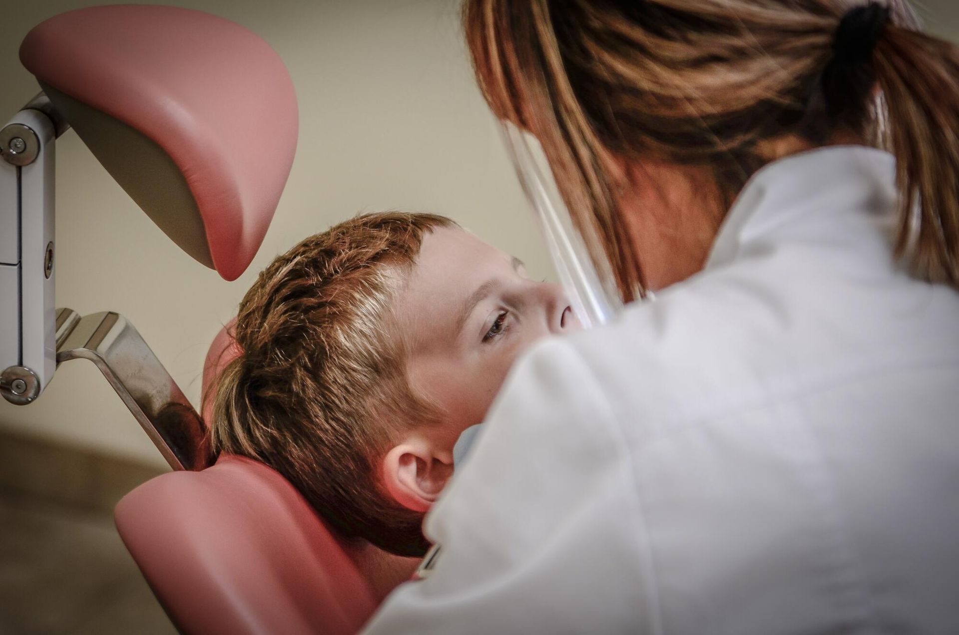 Boy in dentist chair having checkup by a dental professional wearing a white coat.