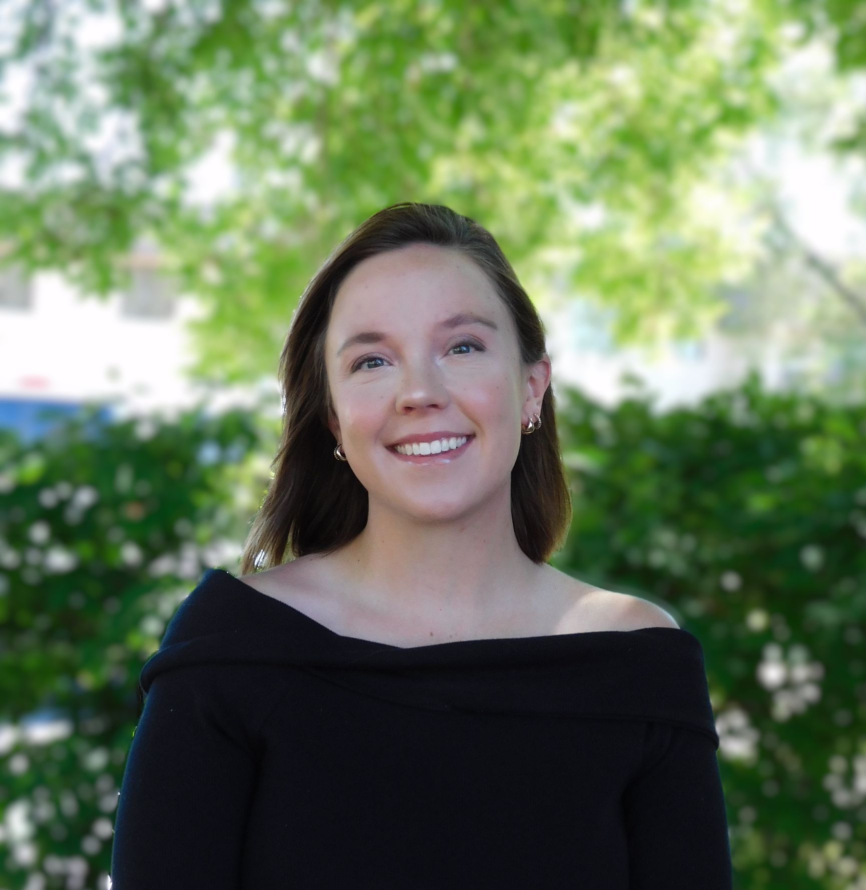 Una mujer con un top negro con hombros descubiertos sonríe para la cámara.