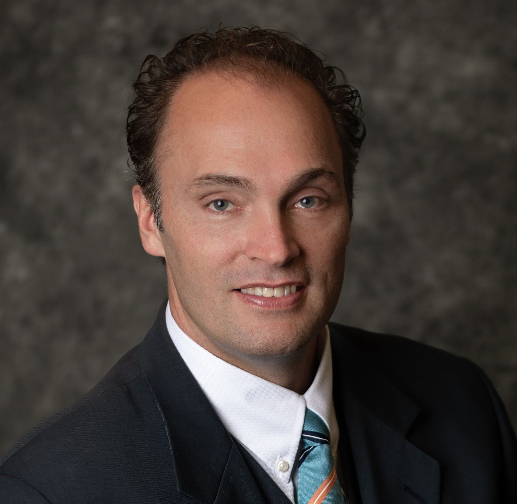 Un hombre con traje y corbata sonríe para la cámara.