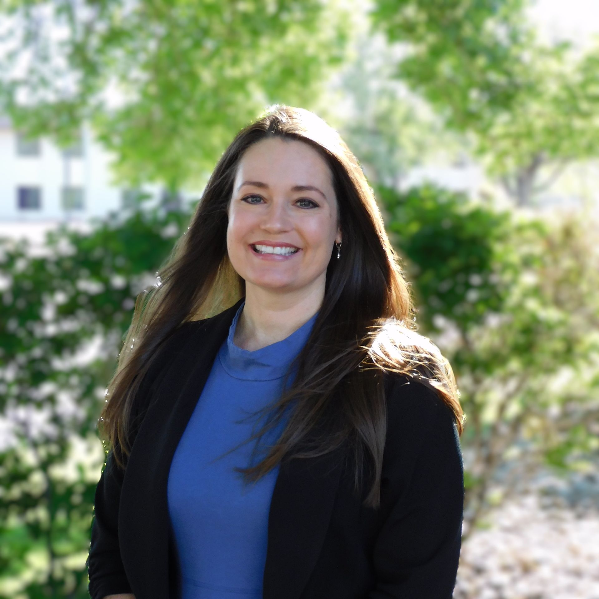 Una mujer con una camisa azul y una chaqueta negra sonríe para la cámara.