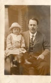 A man in a suit and tie is sitting next to a little girl in a hat.