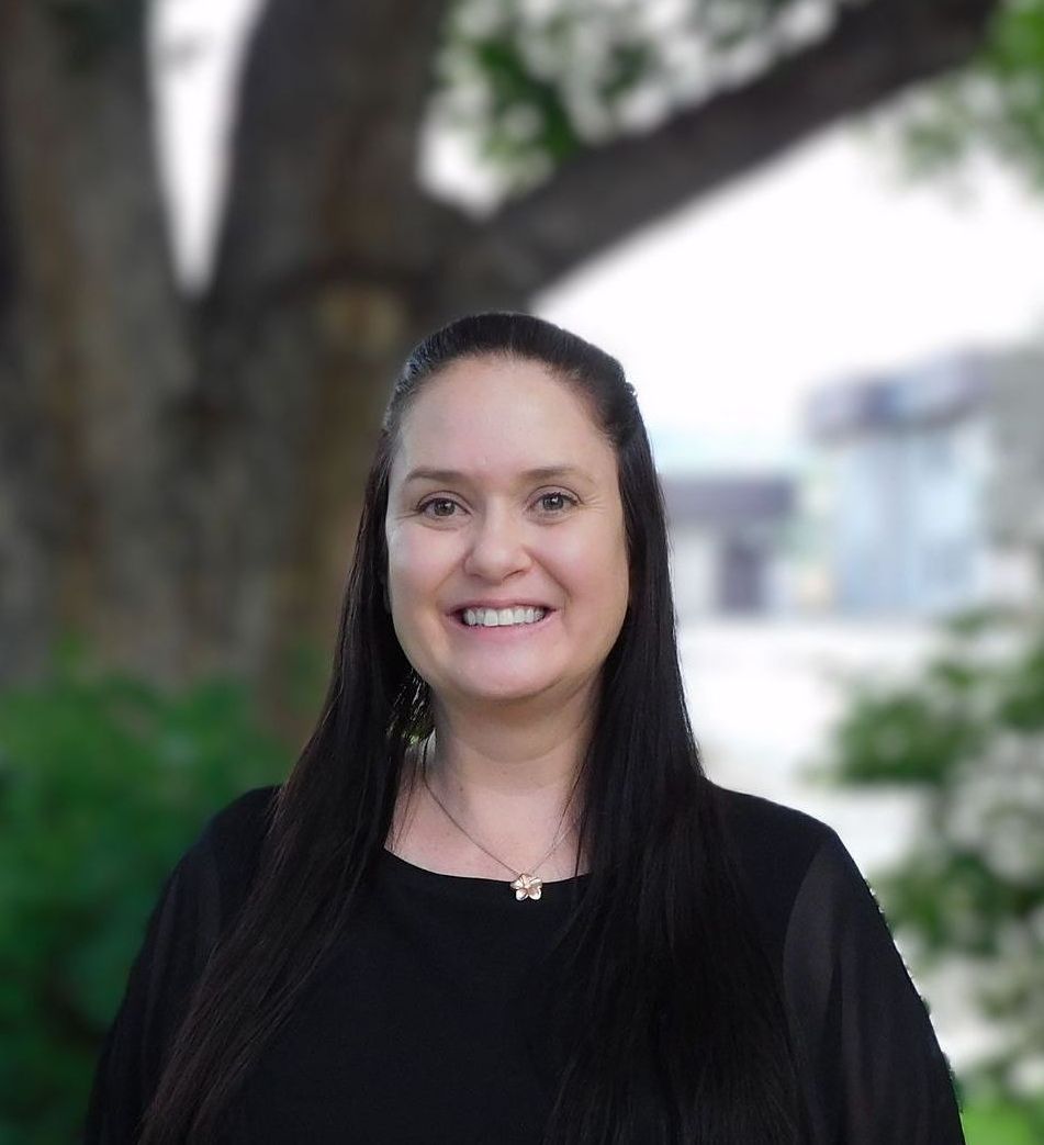 Una mujer con una camisa negra sonríe delante de un árbol.