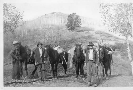 A group of men are standing next to horses on a dirt road.