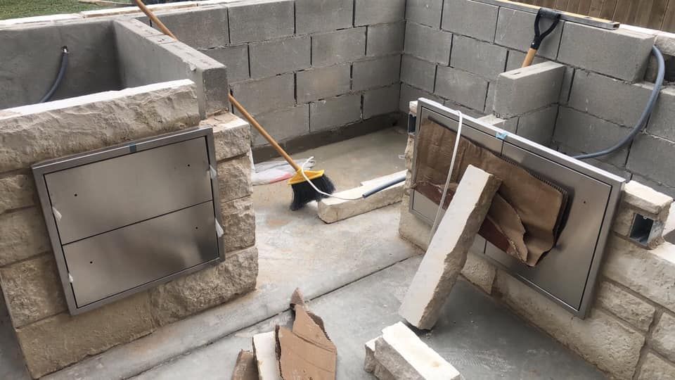 Outdoor kitchen under construction with concrete block and stone. Stainless steel doors installed.