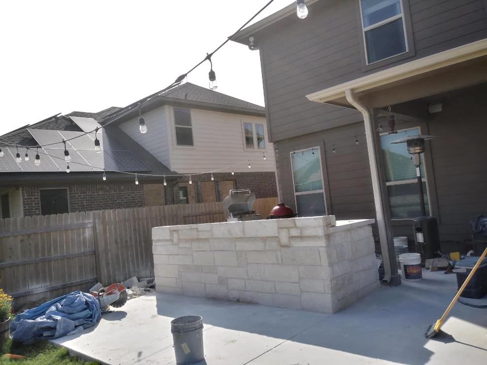 Backyard with stone outdoor kitchen under string lights. Houses in background.