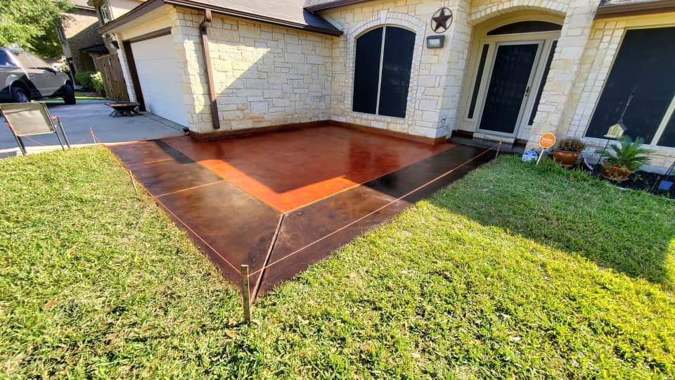 Brown stained concrete patio and walkway bordered by dark brown, in front of a house.