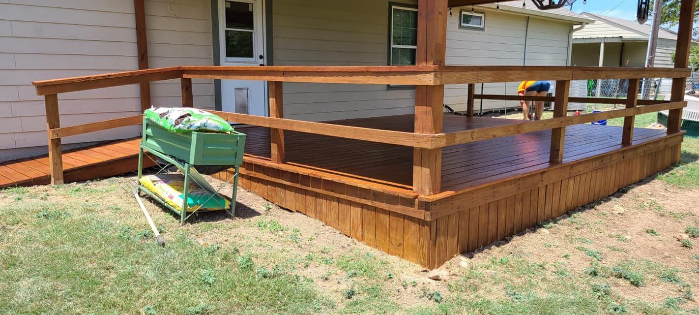 Wooden deck with ramp and railing, green grass, and a green bin. The deck is brown.