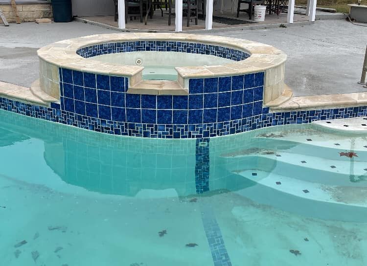 Swimming pool with blue tile hot tub, water, and steps.