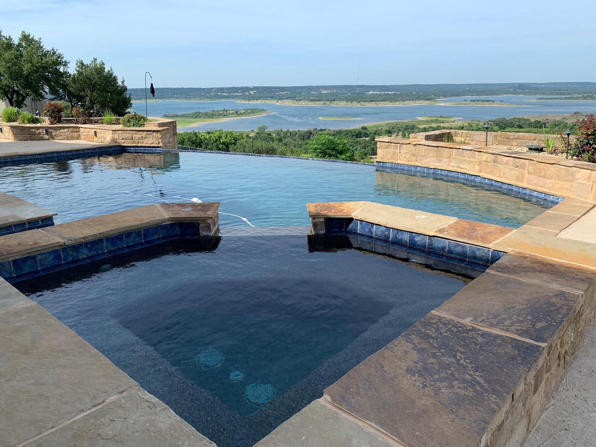 Infinity pool overlooking a lake, with stone walls and blue tile.