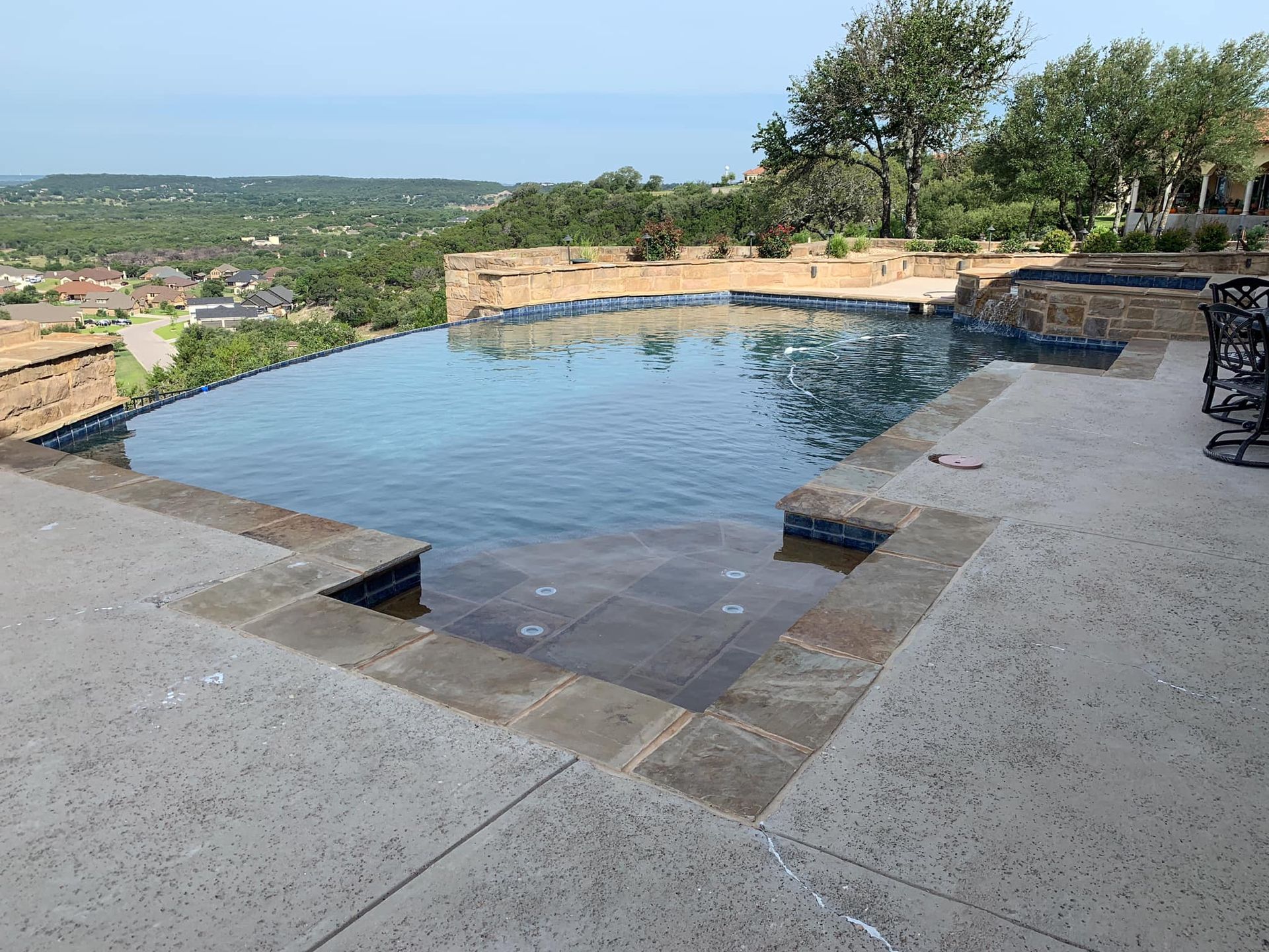 Infinity pool overlooking a city, with stone tile surround and clear water.