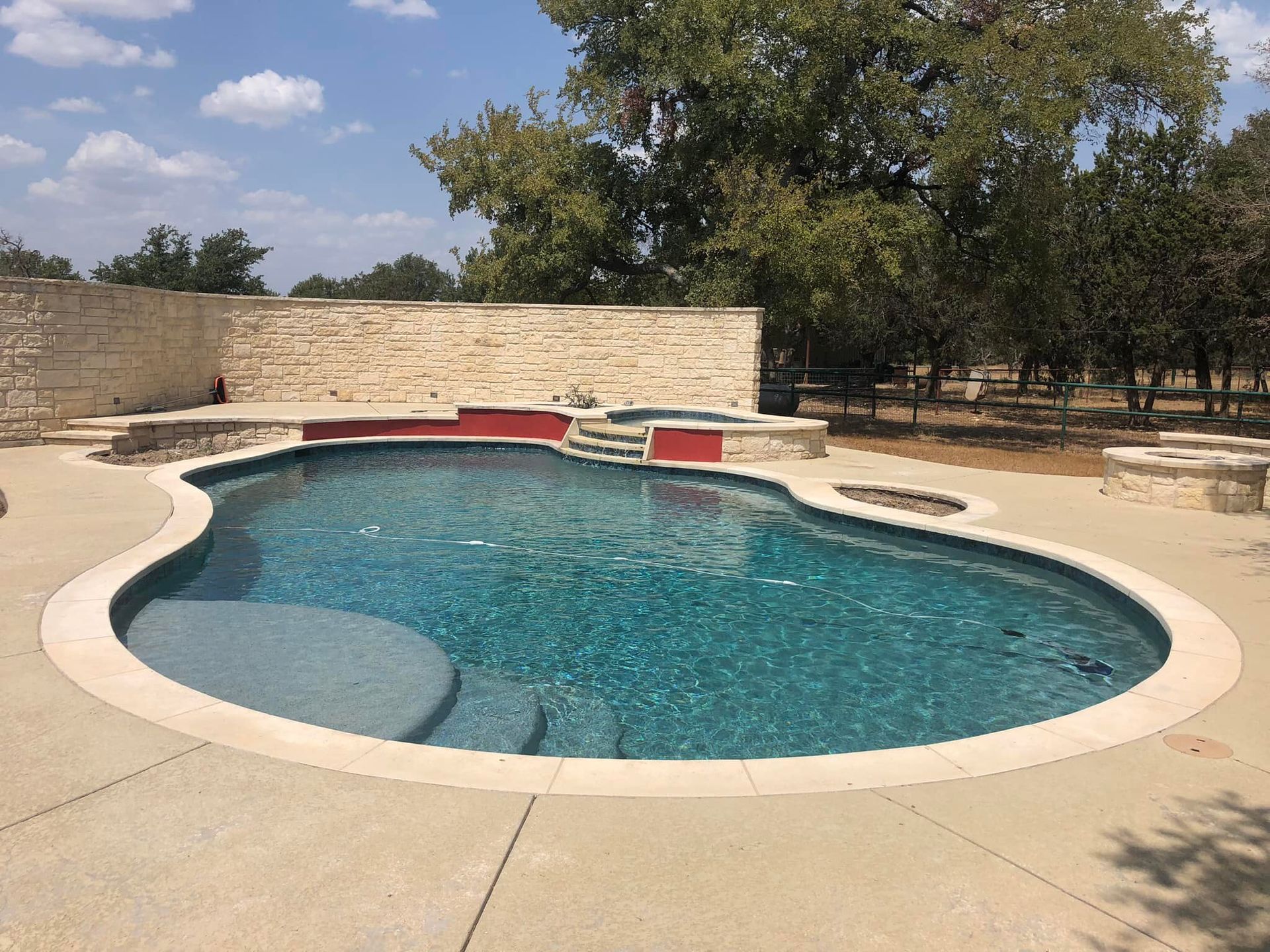 Swimming pool with blue water and stone deck on a sunny day.
