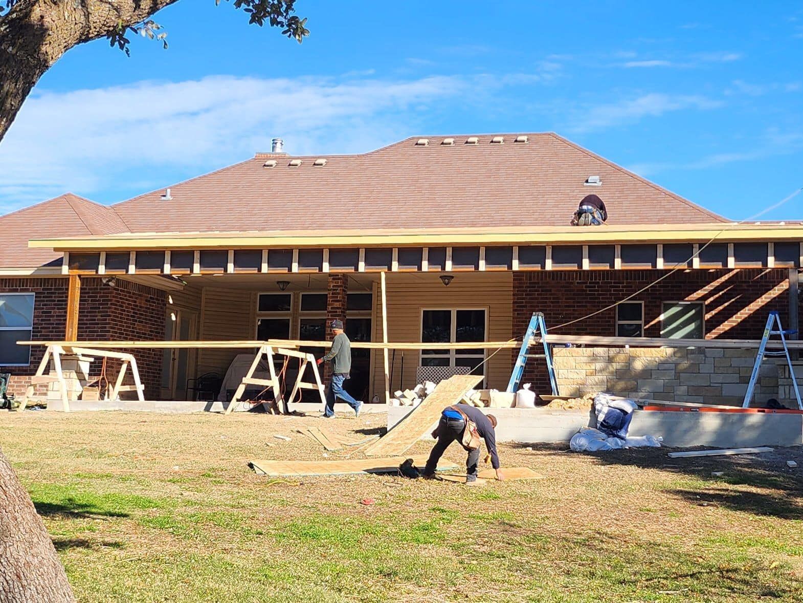 Construction of a covered patio on a house. Workers building, wood framing, sunny day, backyard setting.