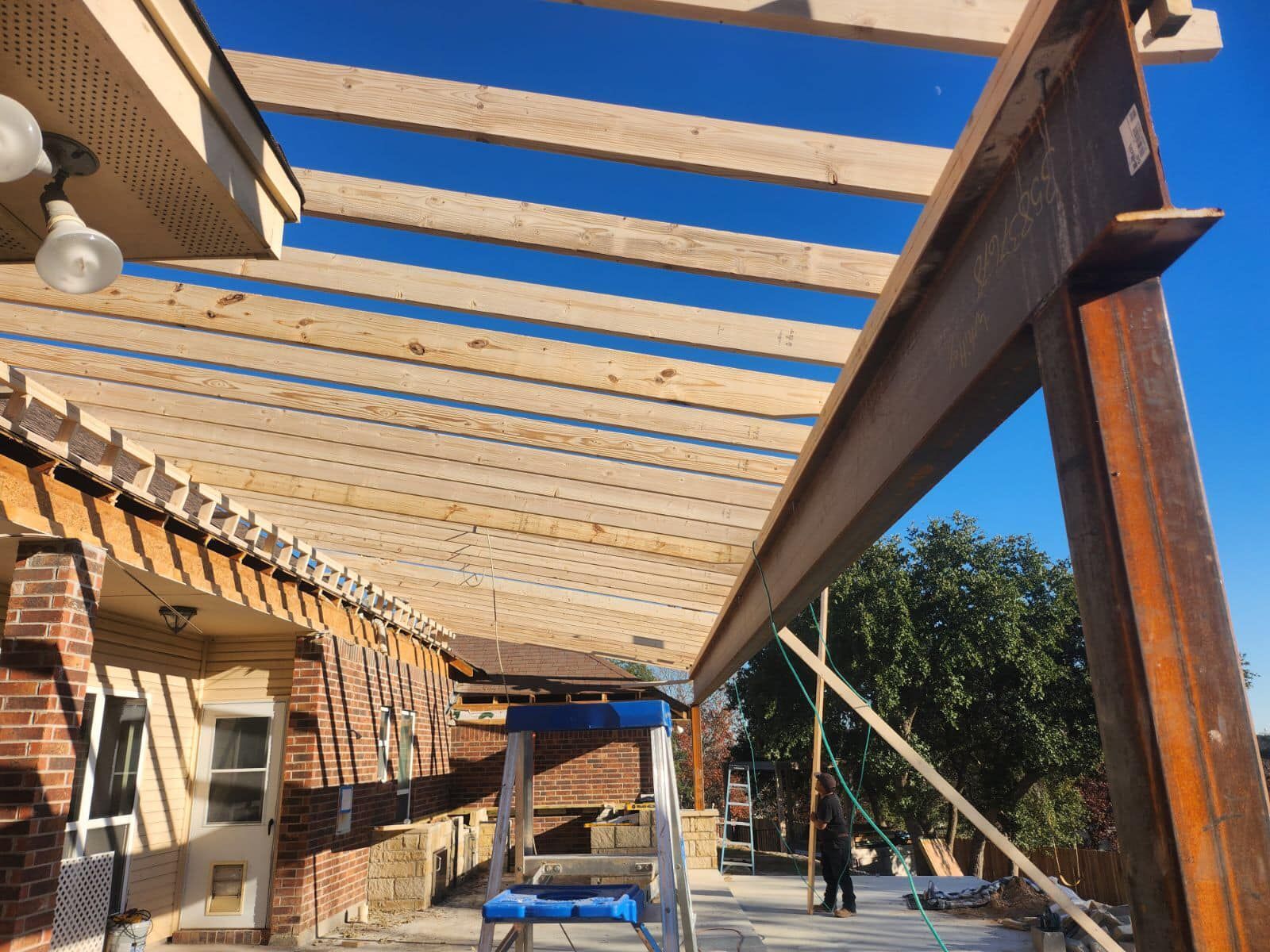 Pergola construction with brown beams and wooden slats against a clear blue sky.