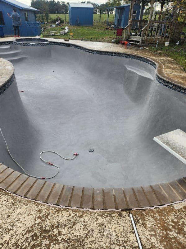 Empty pool with gray concrete interior and brick coping.