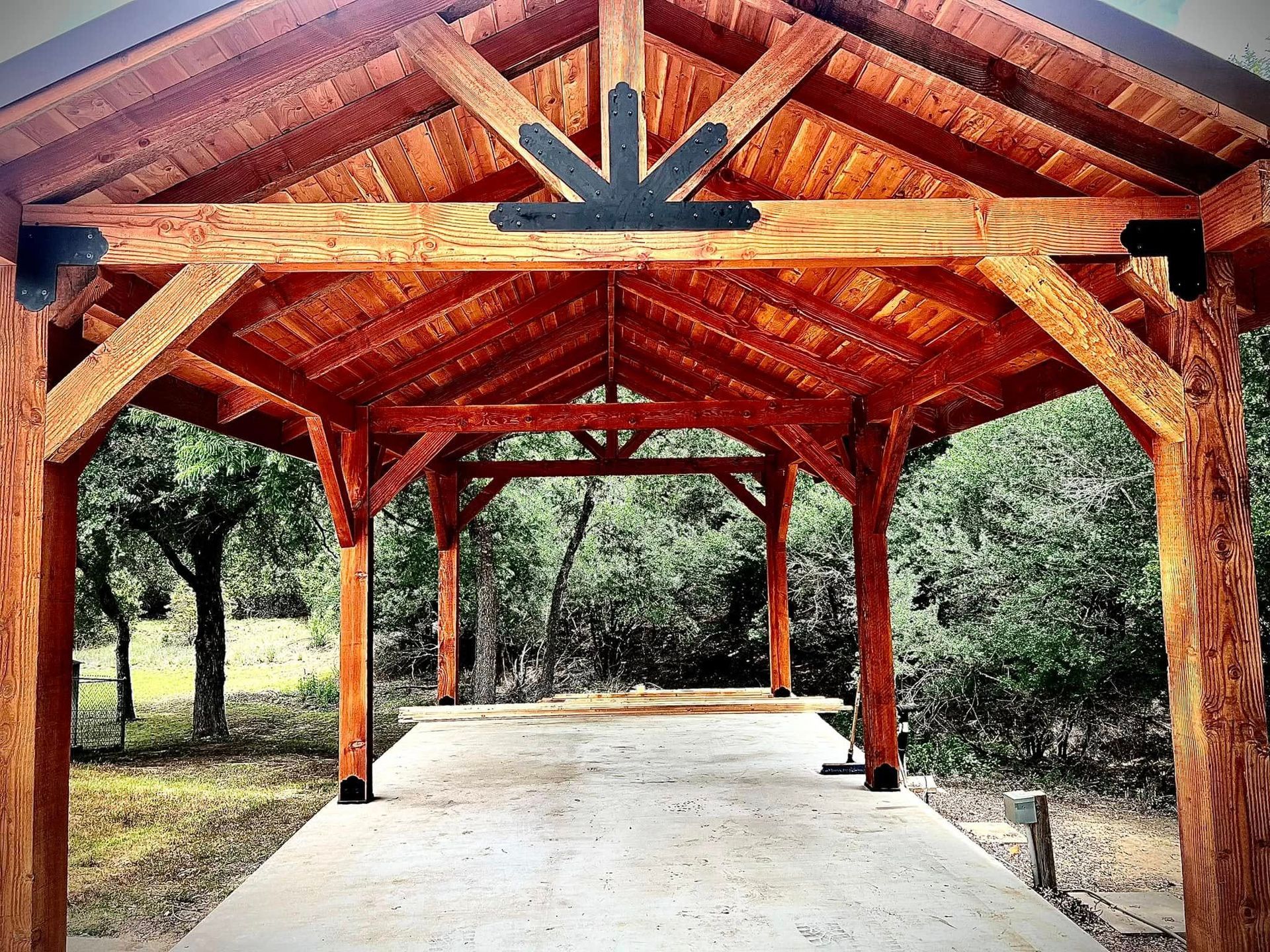 Wooden pavilion with a concrete pathway, trees in the background.
