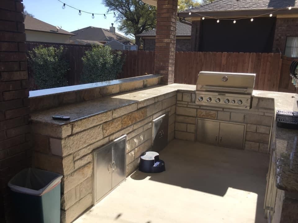 Outdoor kitchen with stone counters, stainless steel grill, and metal storage doors.