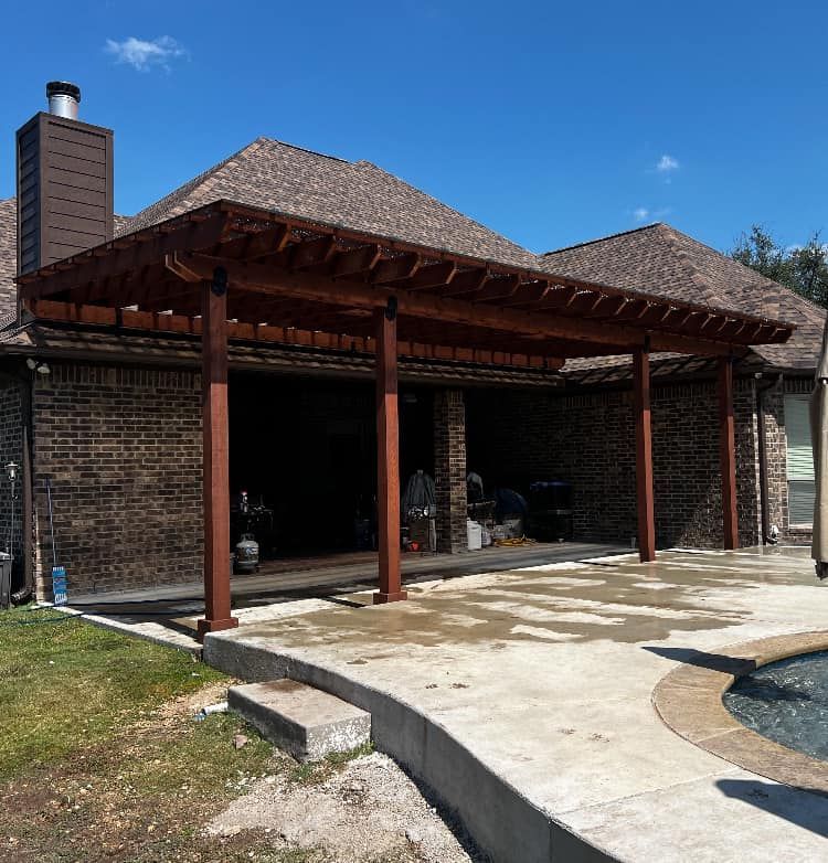 Redwood pergola attached to a brick house with a pool and green lawn on a sunny day.
