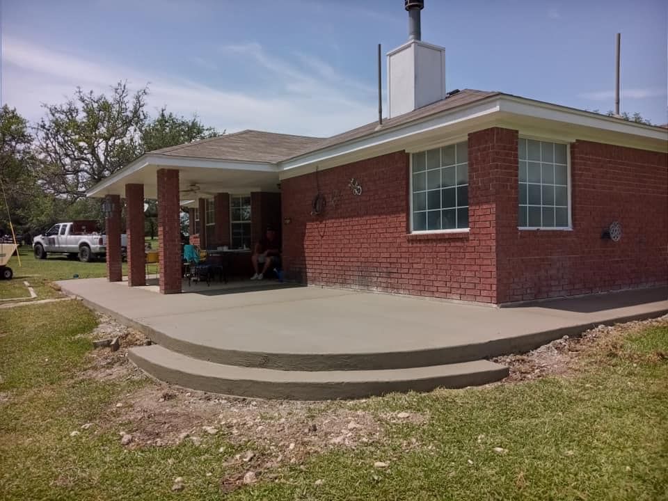 Concrete patio with two steps in front of a brick house with a covered porch.