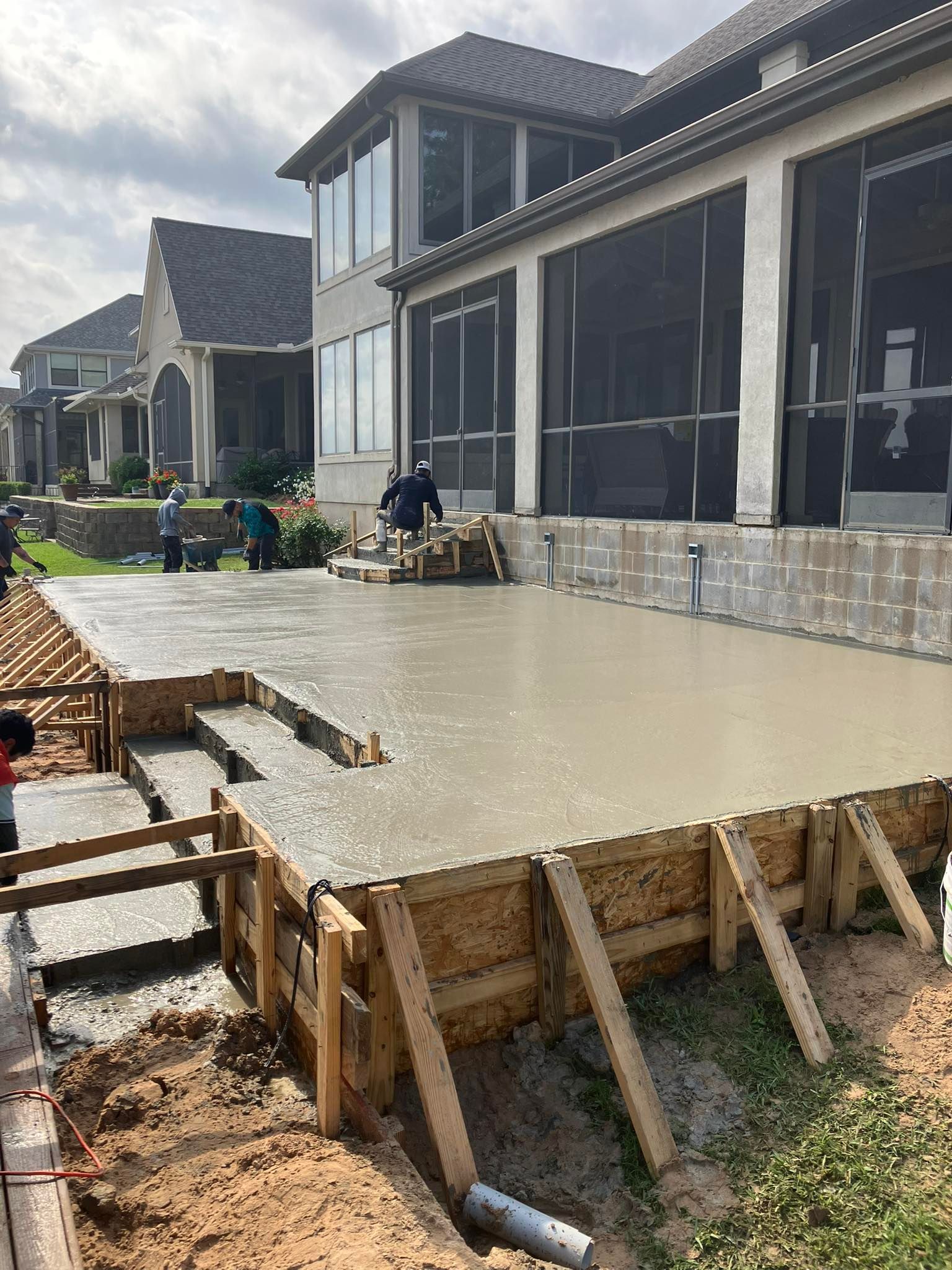 Concrete patio pour with wooden forms, workers, and house in the background.