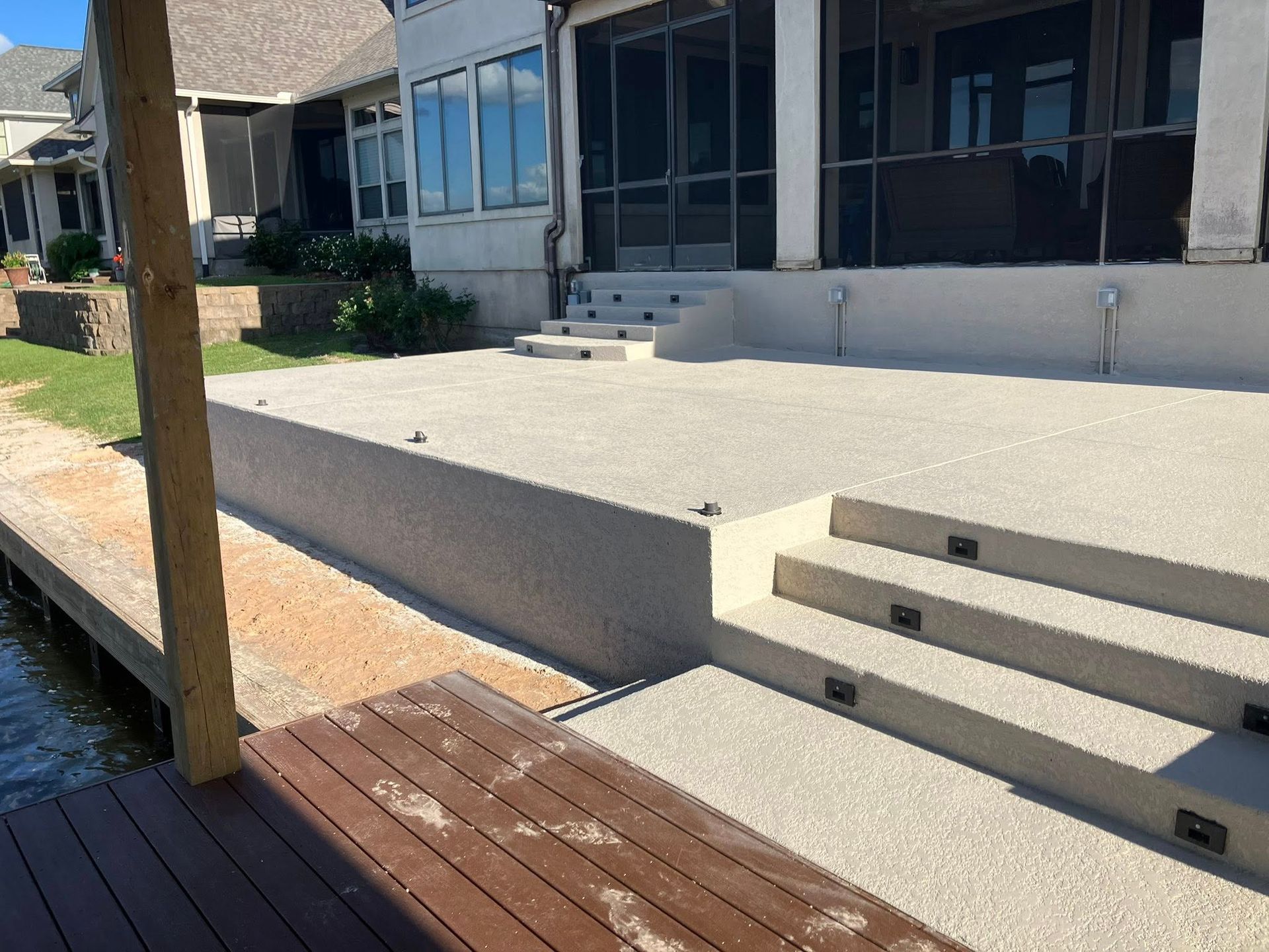 Concrete patio with steps leading to a screened porch, overlooking a dock and water.