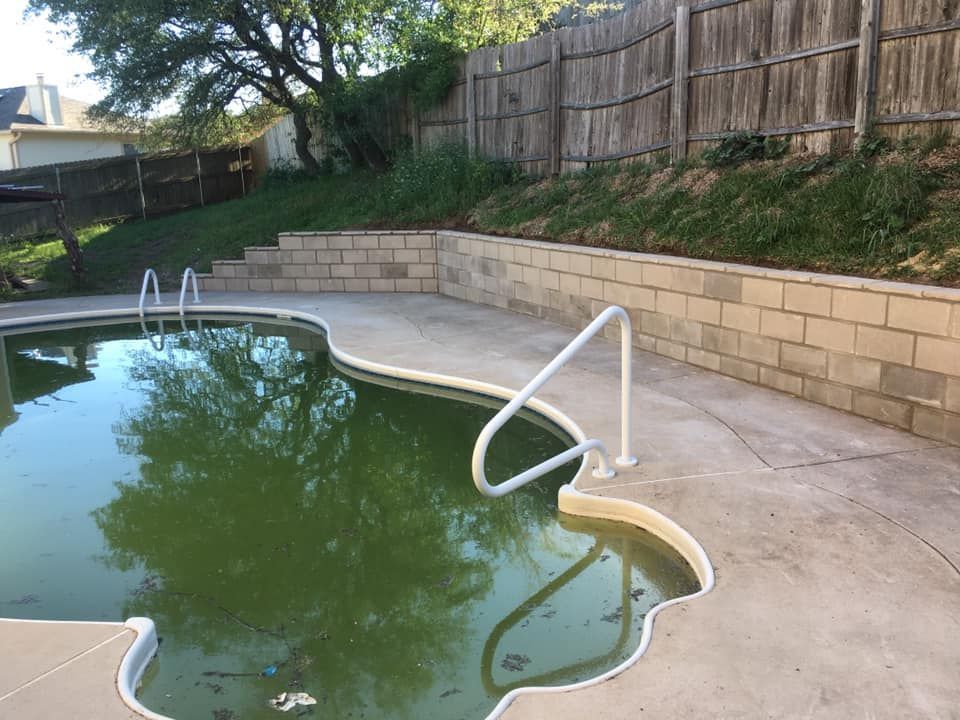 Green, algae-filled swimming pool next to concrete patio and retaining wall.