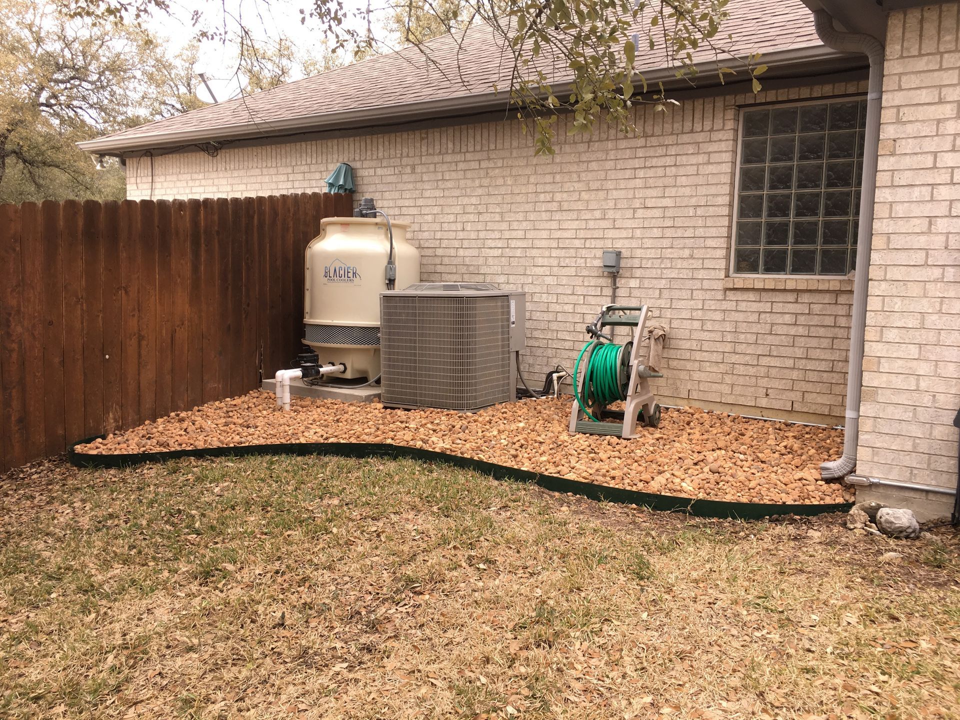 Backyard with brown fence, brick wall, air conditioner, rocks, and hose reel.