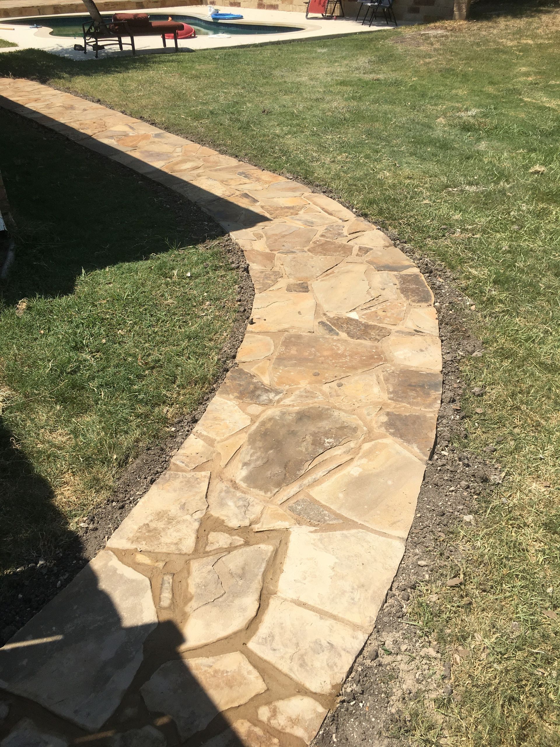 Stone pathway curving through a grassy yard, leading to outdoor seating.