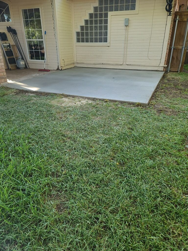 Concrete patio outside a tan house with a grassy lawn in the foreground.