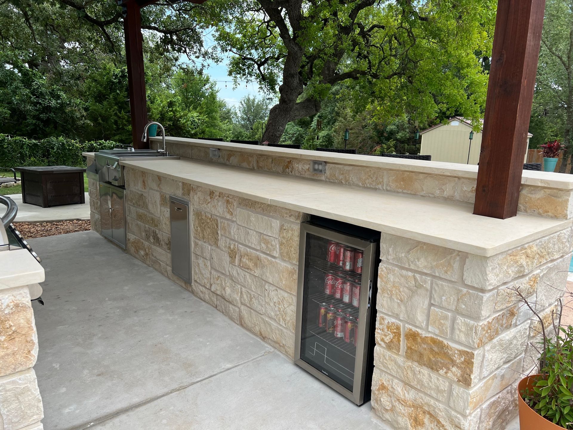 Outdoor kitchen with stone facade, counter, built-in grill, and small refrigerator.