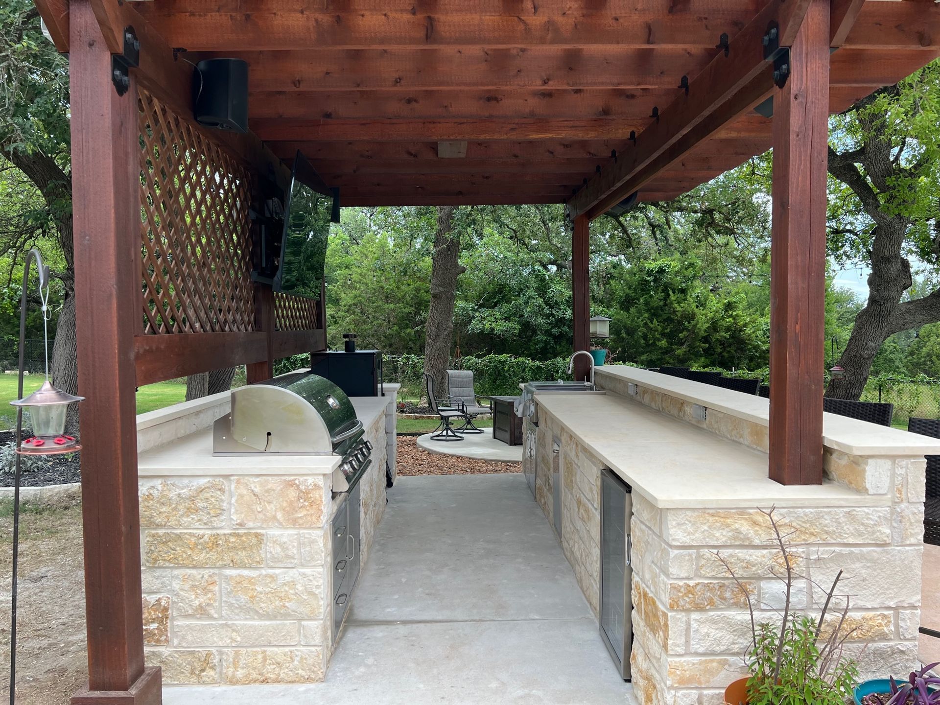 Outdoor kitchen with a wooden pergola, built-in grill, and bar. Stone counters and cabinetry.