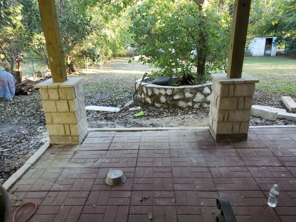 Brick patio with stone pillars and a circular garden bed in a backyard setting.