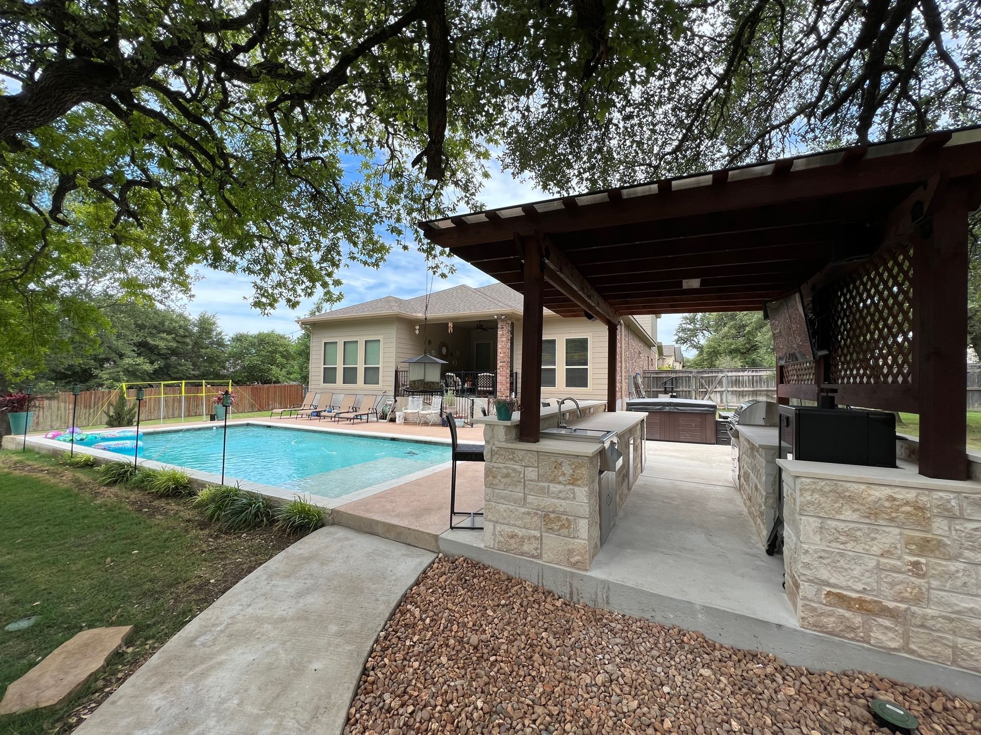 Backyard with pool, outdoor kitchen, and pergola; cloudy day.