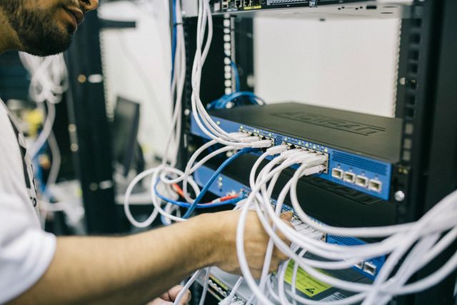 Person working with network cables in a server room. White cables connected to a blue switch.