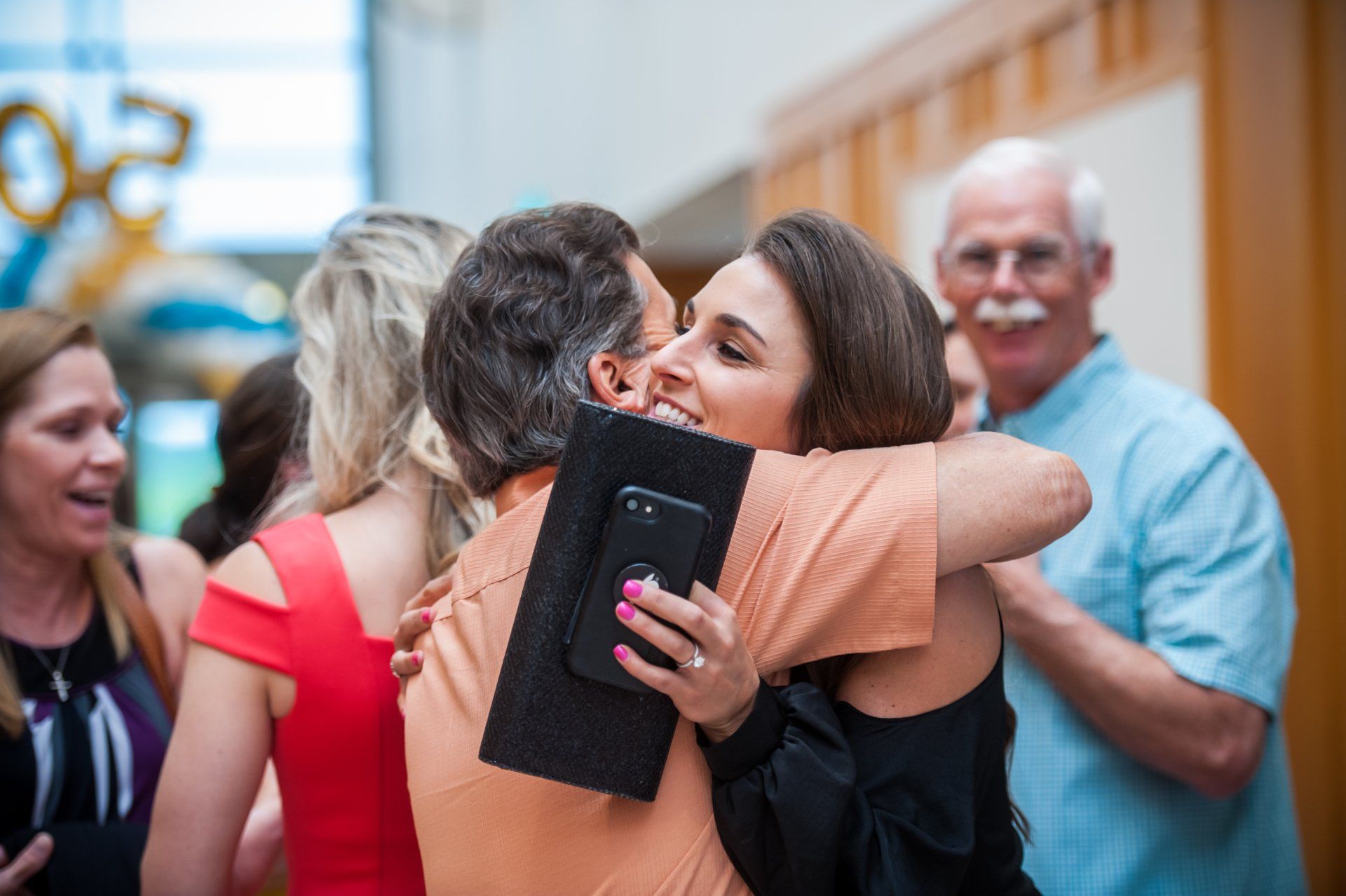 Parkettes 50th  Reunion-a woman is hugging a man while holding a cell phone .