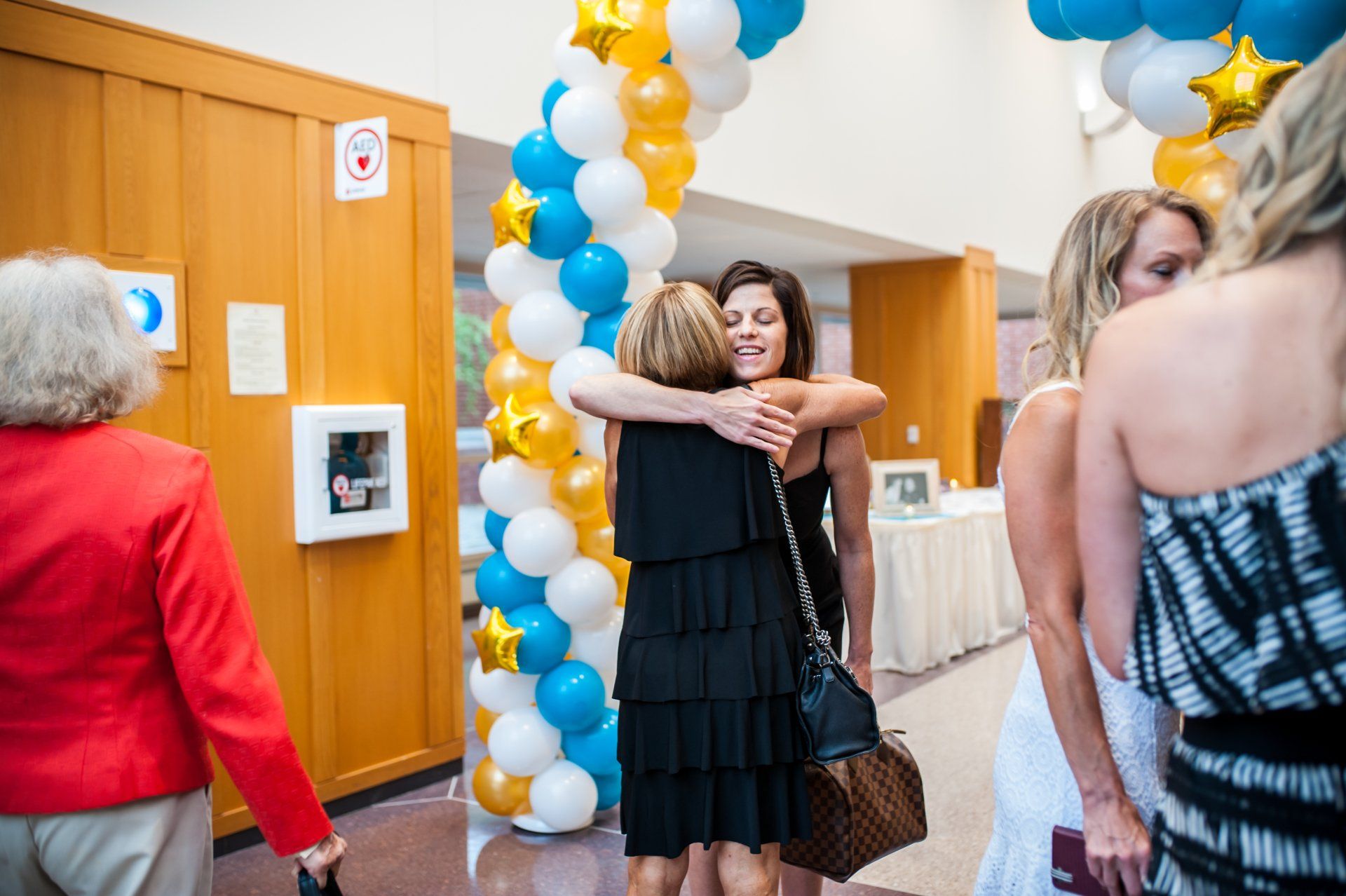 a group of women are hugging each other in front of a balloon arch .