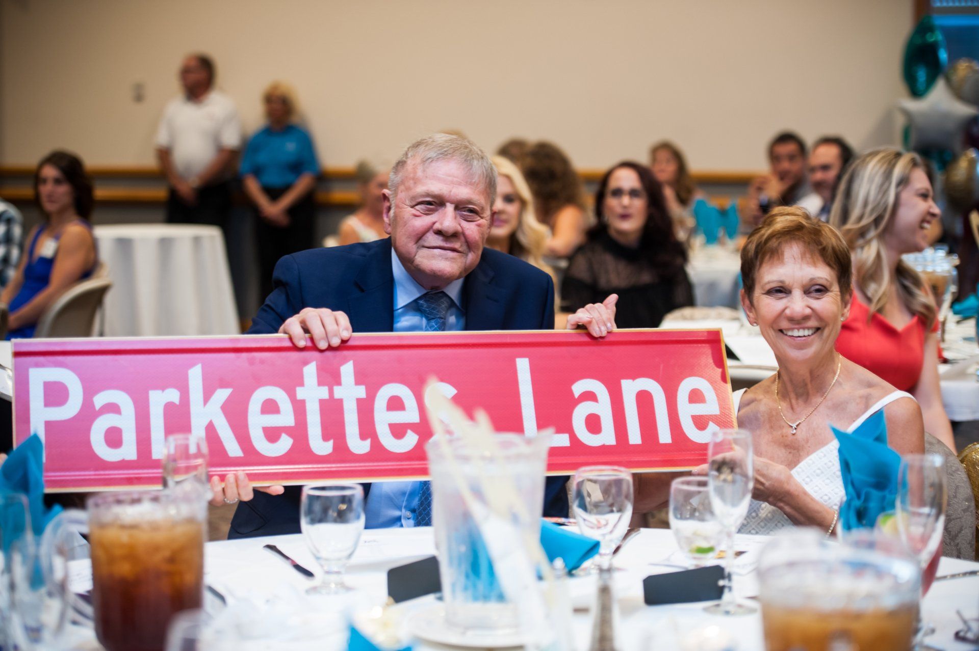 Parkettes 50th  Reunion-a man and woman are sitting at a table holding a sign that says parkette lane .