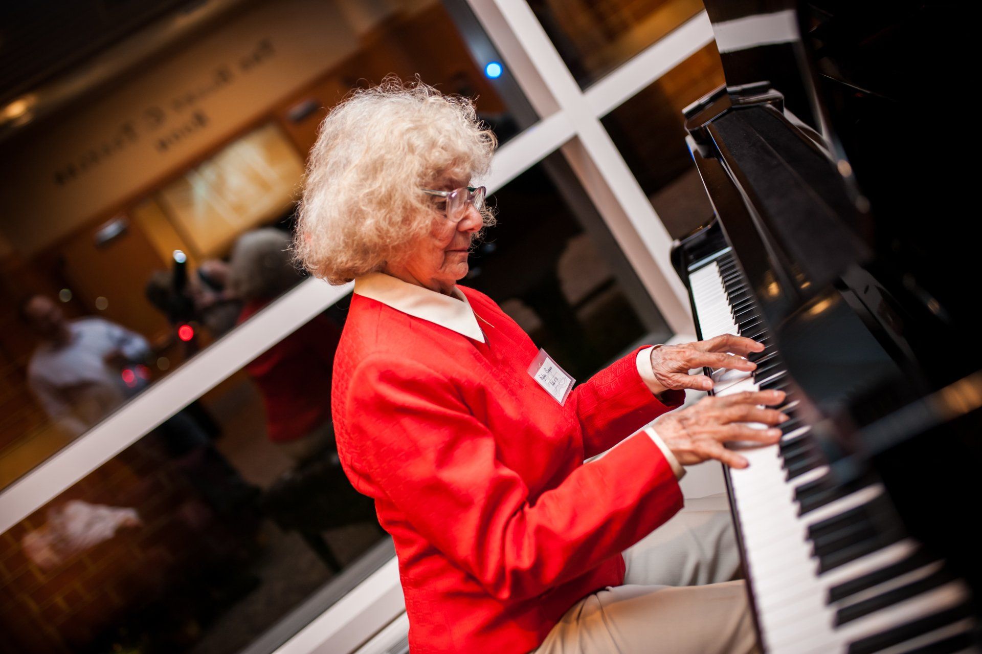 Parkettes 50th  Reunion-a woman in a red jacket is playing a piano in front of a window .