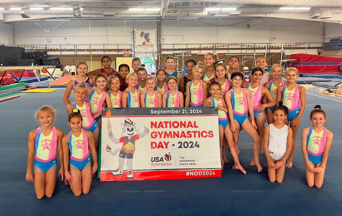 A group of young girls are posing for a picture in a gym for national gymnastics day.