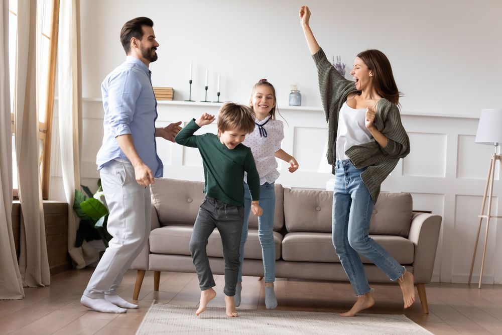 A family is dancing in a living room in front of a couch.